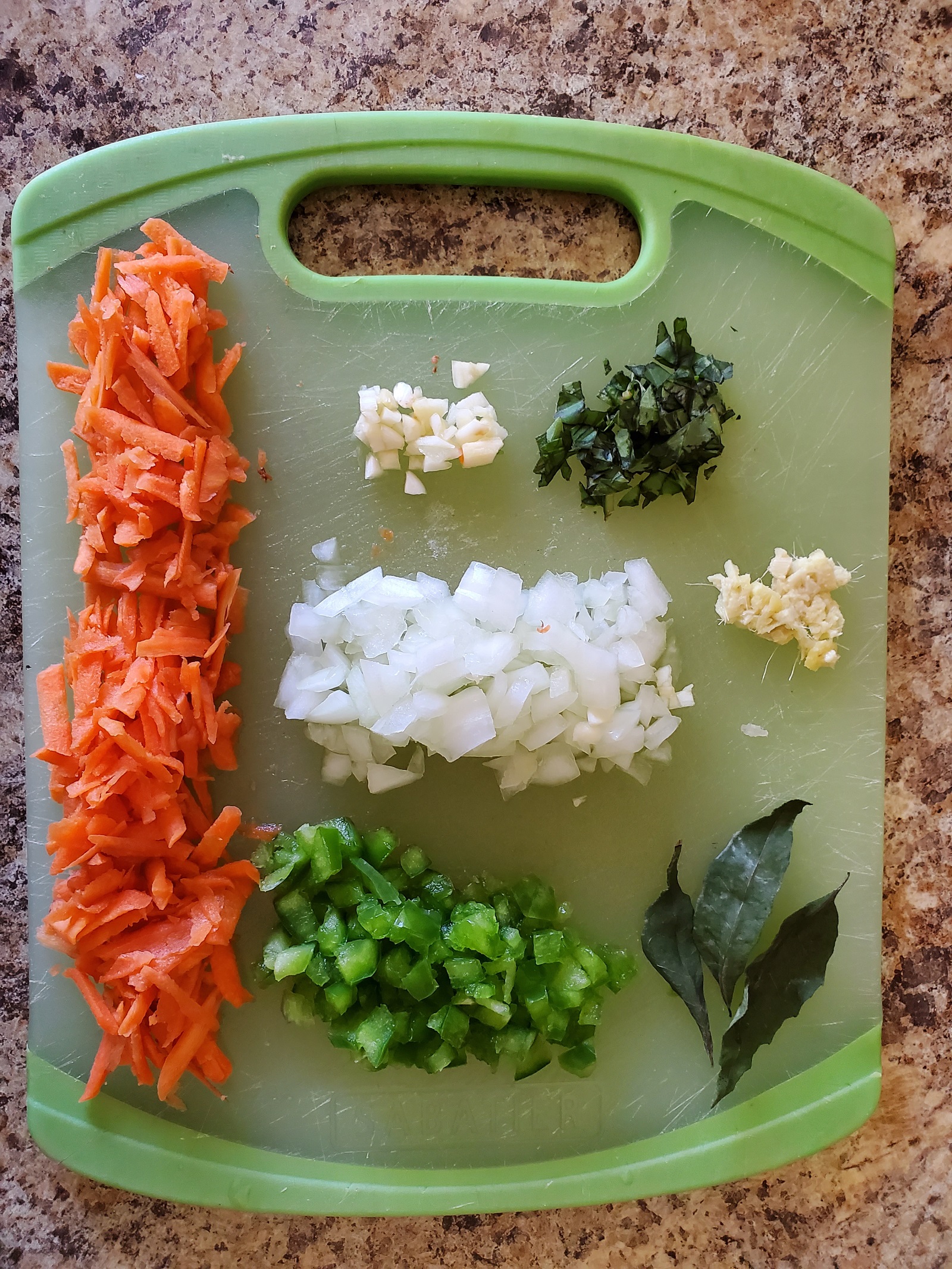 A picture of shredded carrots, minced garlic, rosemary, onions, ginger, bell peppers and some fresh basil on a green cutting board