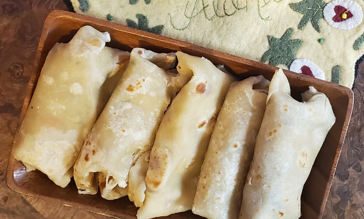 rectangle acacia wood plate with five Fiji chicken curry wrapped in roti sitting atop a hot pad saying aloha and a wooden table