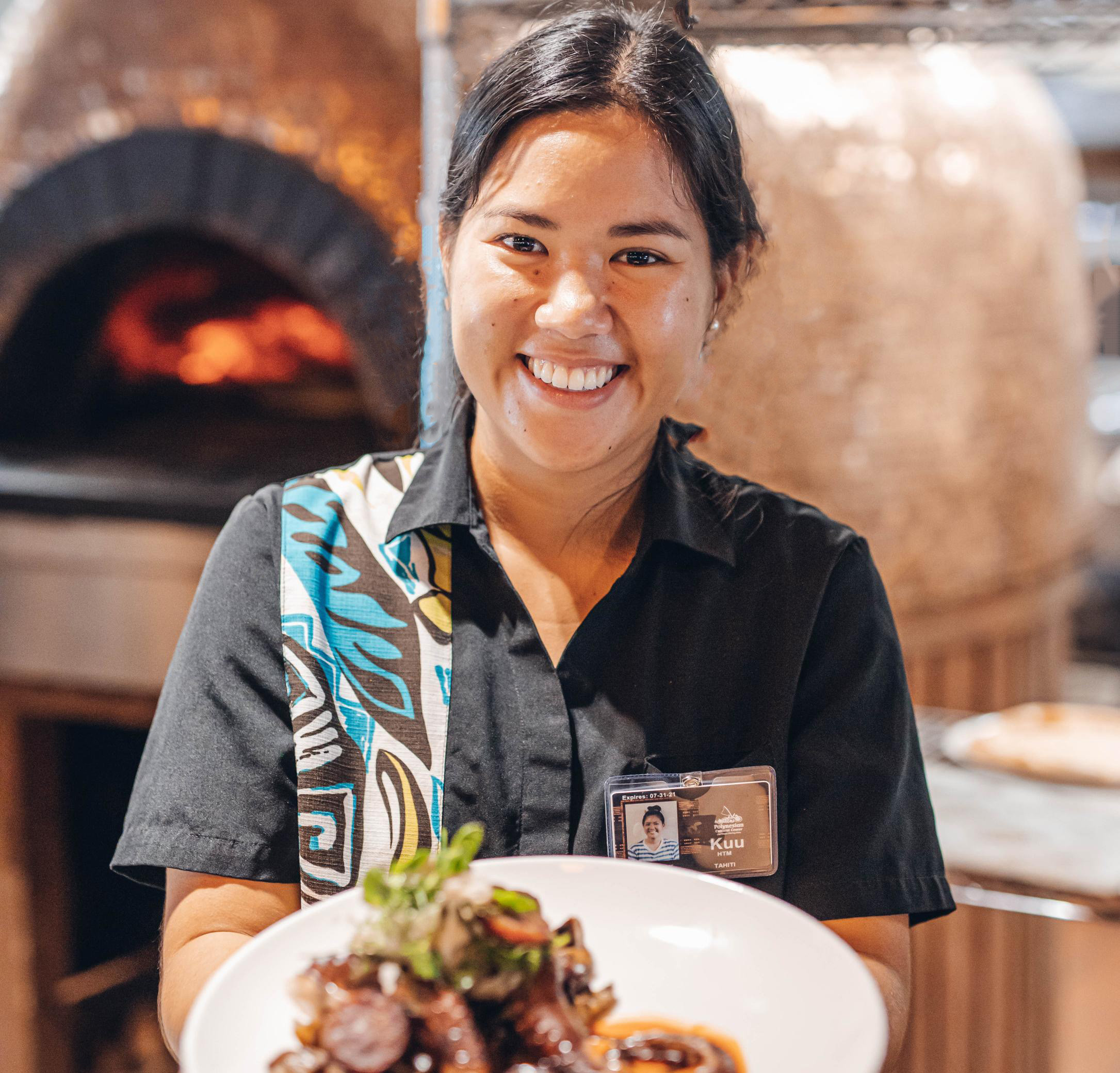 Food server standing in-front of Pounder's Kiawe Oven holding a plate of he'e octopus