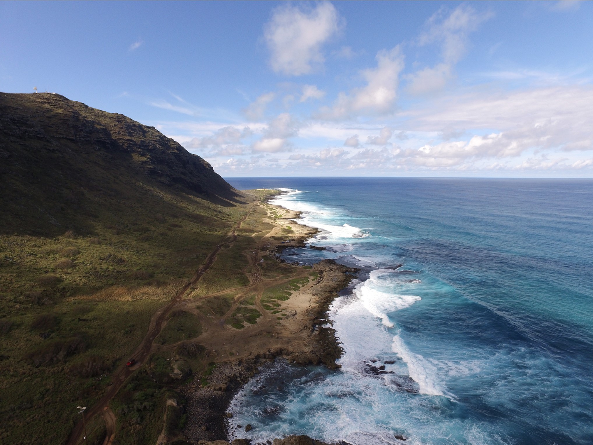 view of rocky island land and deep blue ocean with a towering mountain and low lying shrubbery