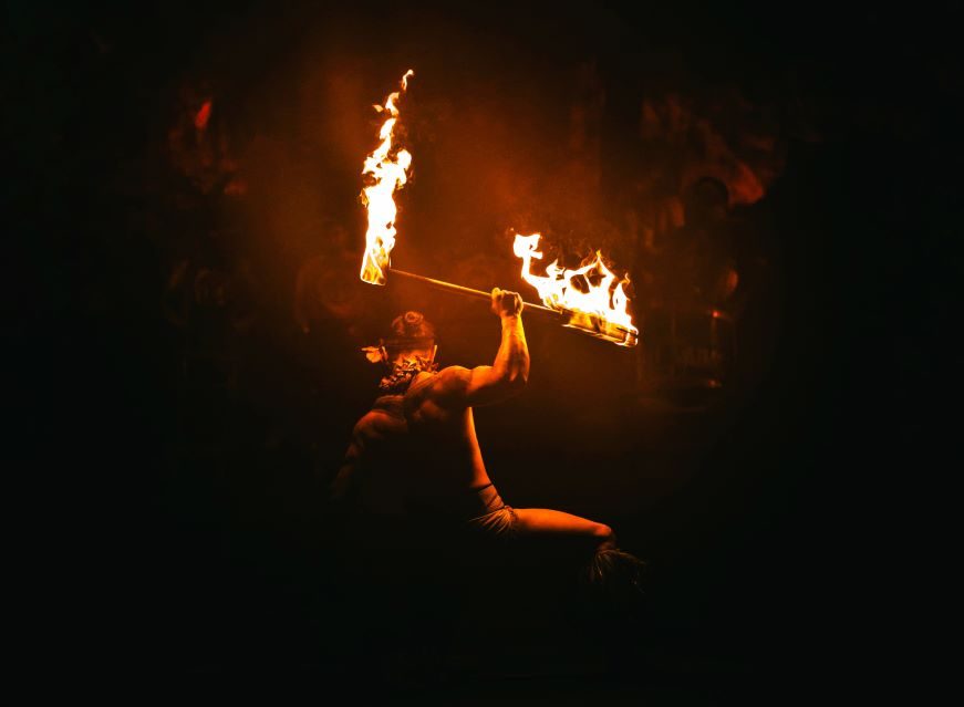 Lopati Leaso kneels while holding his fireknife above him with his back facing the viewer. The 2nd winner of the 29th Annual World Fireknife Championship.