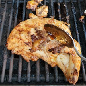photo of grilled huli huli chicken being brushed with sauce with a spoon 