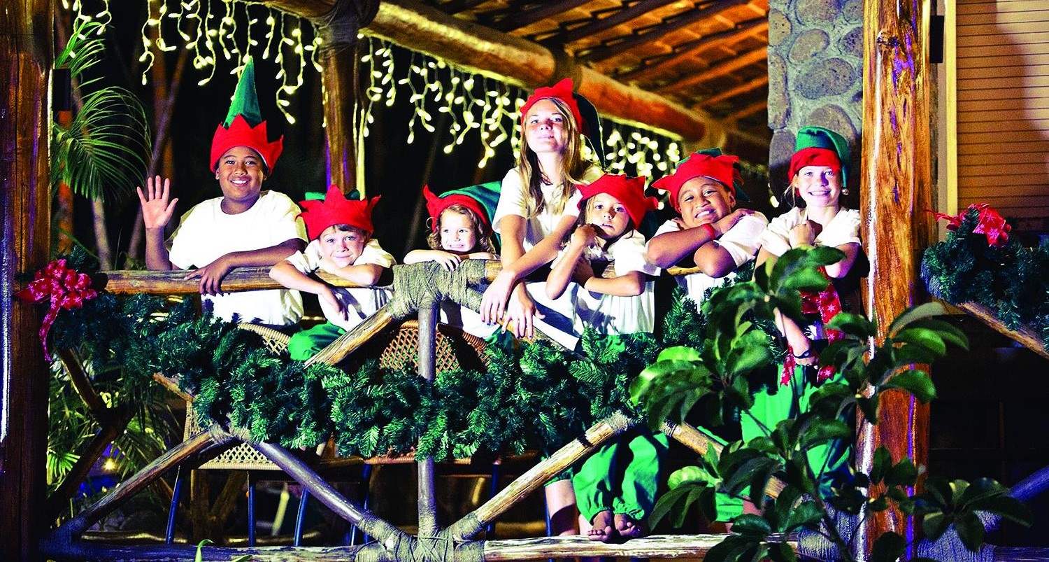 image of 7 kids wearing elf hats and white shirts posing behind the Christmas decor